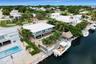 Waterfront property featuring a private boat dock, a thatched-roof tiki hut, mature palm landscaping, and a second-story balcony