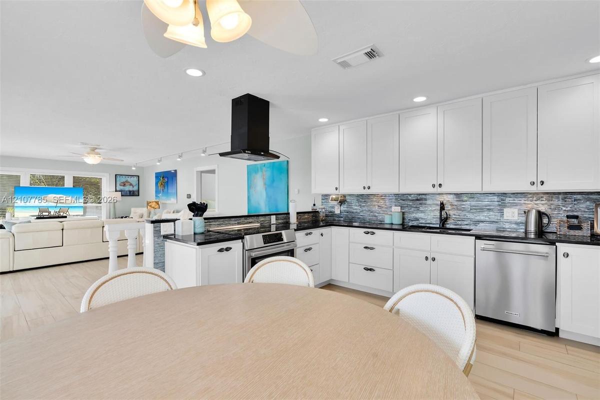 Kitchen featuring white cabinetry, dark countertops, a textured tile backsplash, a stainless steel dishwasher, and a matte black wall-mounted range ho