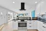 Kitchen featuring white cabinetry, dark countertops, a tiled backsplash, stainless steel oven, and a black chimney-style range hood