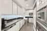 Galley kitchen featuring white cabinetry, black granite countertops, herringbone-patterned tile backsplash, stainless steel appliances