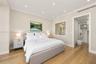 Neutral-toned bedroom featuring light wood-finish flooring, recessed ceiling lighting, crown molding, and an interior window to bathroom with switchab