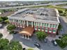 Three-story commercial building featuring a curved metal portico entrance, masonry facade with multi-pane windows, and paved surface parking