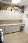 Built-in cabinetry featuring light-toned doors, extensive countertop workspace, wood-finish flooring, and drop-ceiling lighting