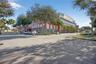 Commercial building exterior featuring a multi-story facade, covered porte-cochère, expansive paved surface parking, and mature palm and shade tree la