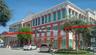 Commercial building exterior featuring a multi-story facade with expansive glass windows, structured red metal awnings, and a covered portico entrance