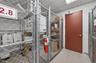 Enclosed storage area featuring galvanized chain-link partitioning, integrated wire shelving, a steel door, and a drop ceiling