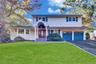 Two-story exterior featuring shake-style siding, a covered arched entryway, a double-car garage, and multi-pane windows with decorative shutters