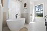 Freestanding soaking tub in the primary bath with tile up half of the surrounding wall with large window for natural light and embracing the privacy o