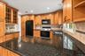 A stylish blend of dark stone countertops, light wood-finish cabinetry, and sleek black built-in appliances creates a modern, inviting kitchen, comple