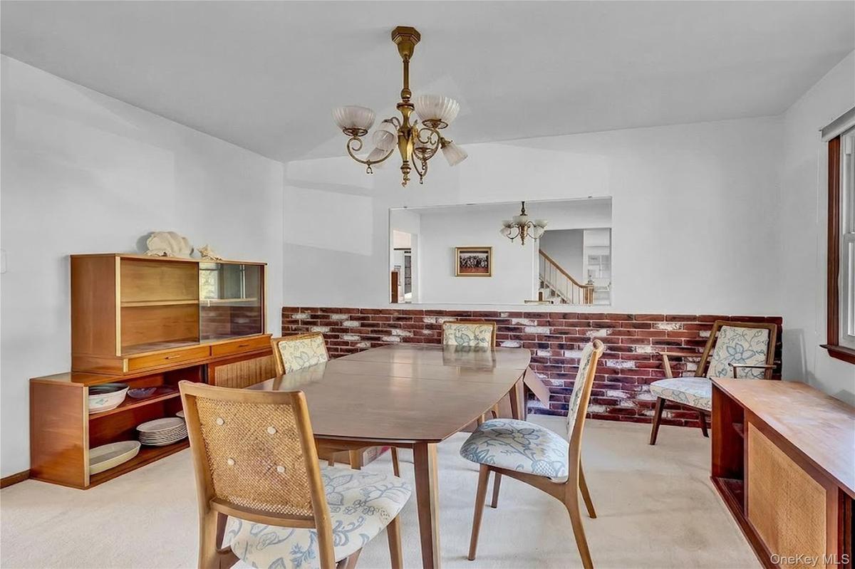 Dining area featuring an exposed brick accent wall, a large rectangular wall cutout, and a traditional multi-arm chandelier