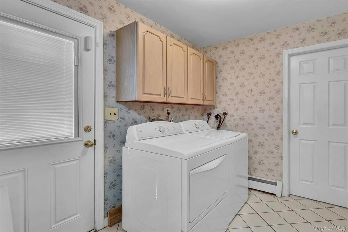 Utility space featuring light-toned wood-finish upper cabinetry, tiled flooring, and a six-panel door