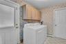 Utility space featuring light-toned wood-finish upper cabinetry, tiled flooring, and a six-panel door