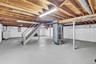 Unfinished lower level featuring exposed wood-beam ceiling construction, painted concrete flooring, structural steel support columns, and interior sta