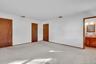 Spacious room featuring neutral carpeting, three solid wood interior doors, and an entry to an attached bathroom with a wood vanity and vanity mirror