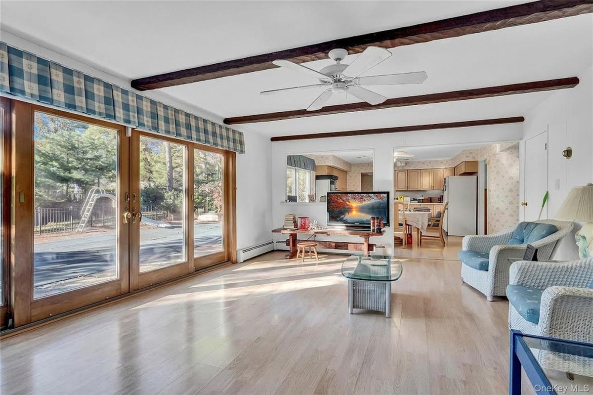 Living space featuring wood-finish flooring, exposed ceiling beams, a ceiling fan, and expansive glass sliding doors