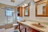 Bathroom featuring a double-sink vanity with wood-finish cabinetry, integrated countertop with dual basins, a glass-enclosed shower and tub combinatio