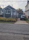 Dark-toned horizontal siding exterior featuring a front-facing wood deck with white railings, a detached garage, and a concrete driveway