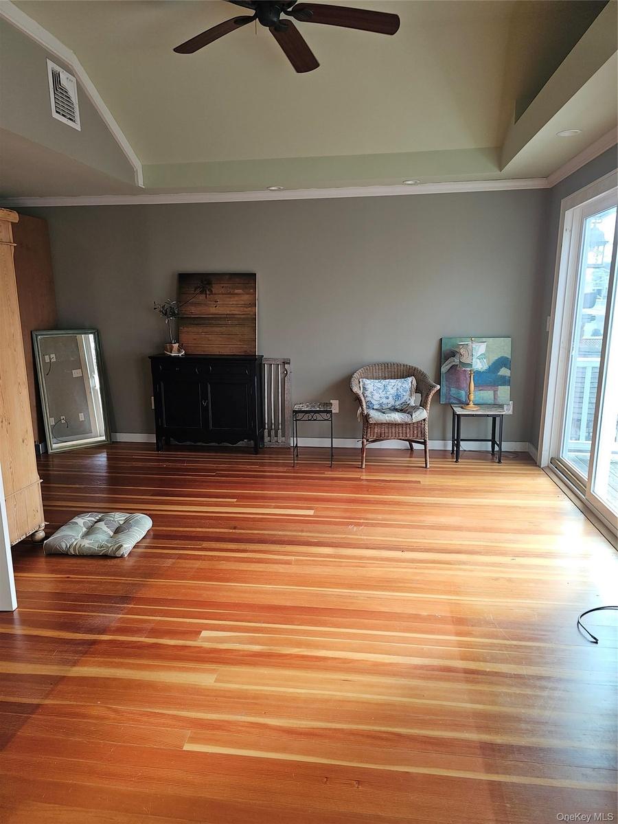 Vaulted ceiling featuring a central paddle fan, wood-finish flooring, and glass sliding doors
