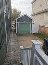 Detached garage featuring vertical siding, concrete driveway, and white vinyl privacy fencing