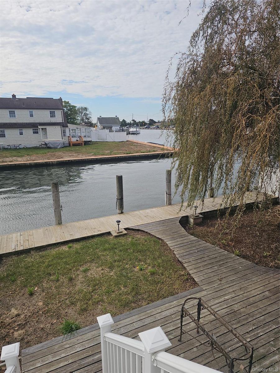Waterfront property featuring a wood-plank deck, a private bulkhead dock, and mature weeping willow tree
