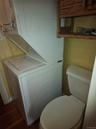 Stacked white laundry center, porcelain toilet, and wall-mounted wooden shelving unit featuring wood-finish flooring