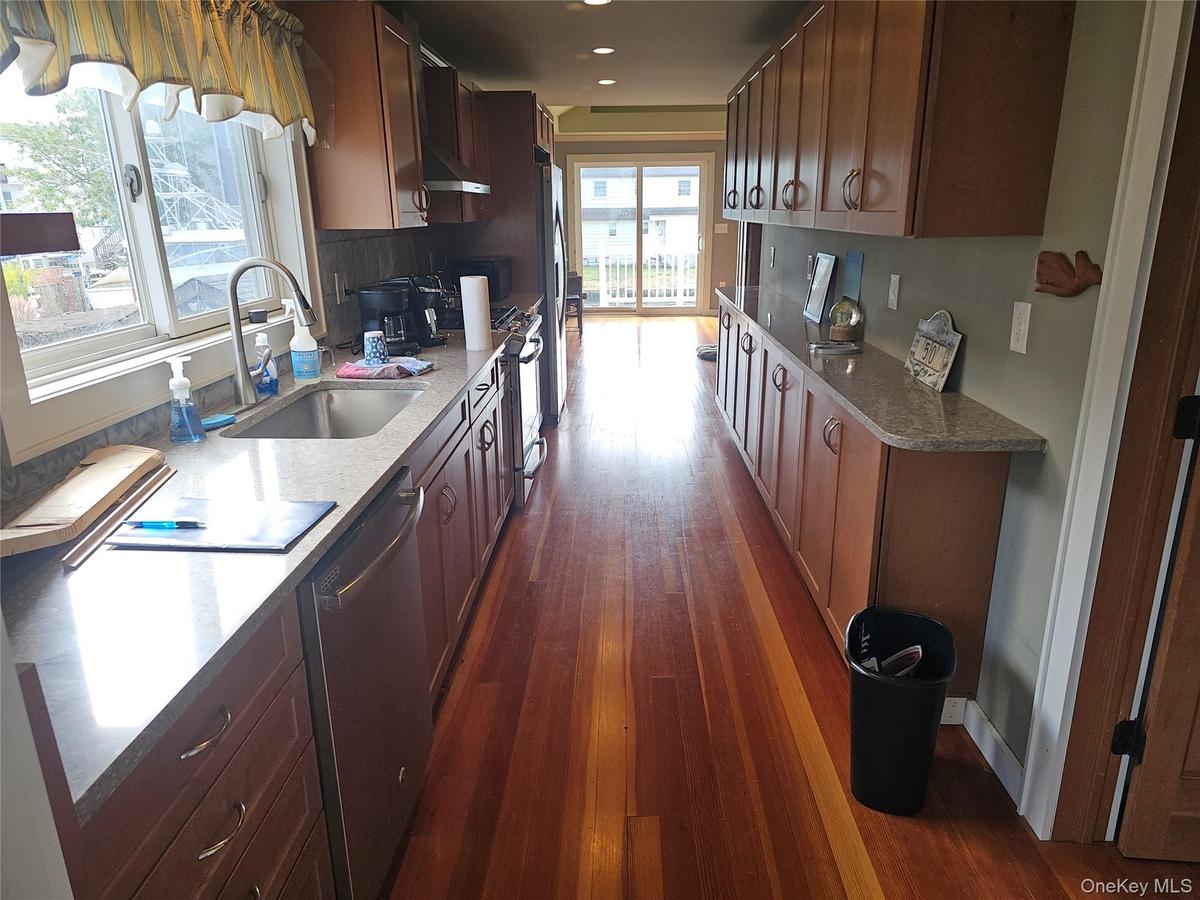 Galley-style kitchen featuring wood-finish flooring, solid-surface countertops, wood cabinetry, stainless steel sink with high-arc faucet, and sliding