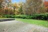 Paver patio featuring a raised timber retaining wall, grass lawn, and mature woodland backdrop
