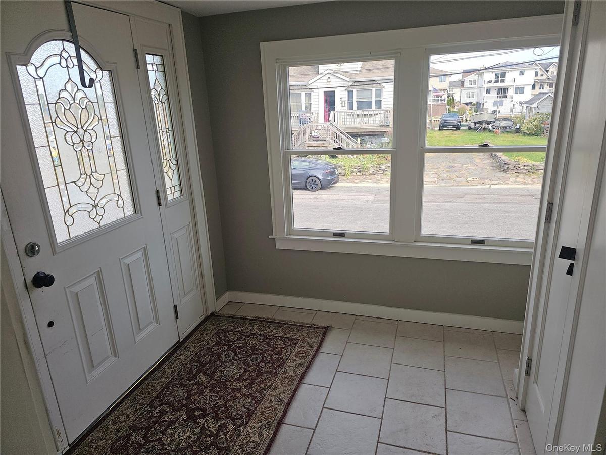 Entryway featuring a white exterior door with decorative glass inserts, ceramic tile flooring, and large windows with white trim