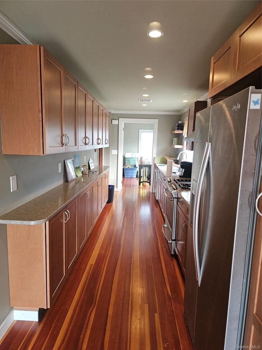 Kitchen featuring extensive wood-finish cabinetry, stone-style countertops, wood-finish flooring, recessed lighting, and stainless steel appliances