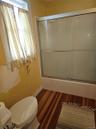 Bathroom featuring wood-finish flooring, a white porcelain toilet, and a shower enclosure with sliding glass doors and a metal frame