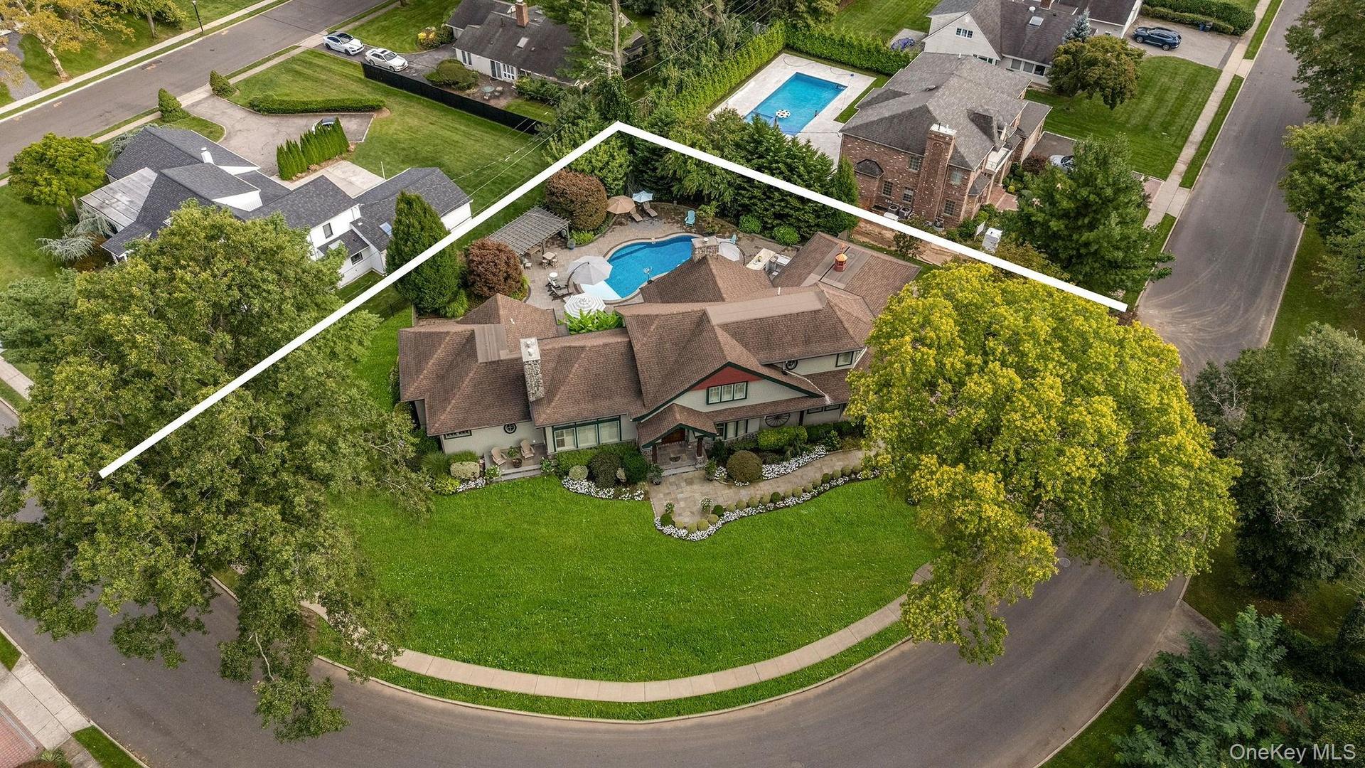 Aerial perspective of a multi-gabled residence featuring a concrete driveway, multi-level shingled roof, stone-accented exterior, and a backyard swimm