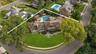 Aerial perspective of a multi-gabled residence featuring a concrete driveway, multi-level shingled roof, stone-accented exterior, and a backyard swimm