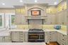 Custom-painted cabinetry featuring glass-front upper displays and a decorative hood enclosure, professional-grade dual-fuel range, farmhouse sink with