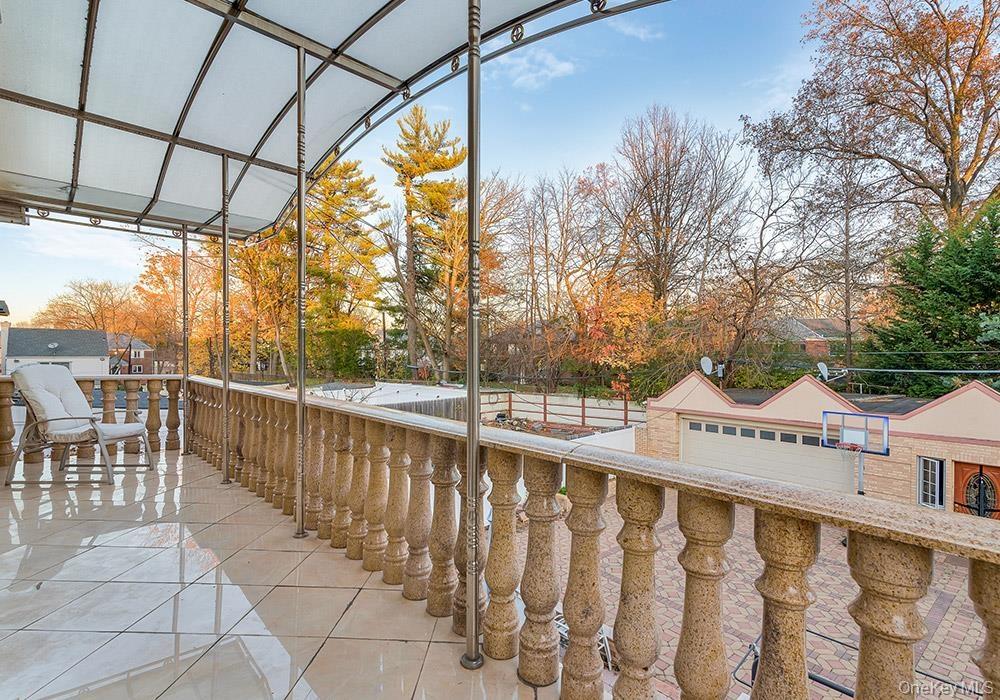Covered terrace featuring stone-finish balustrades, large-format tile flooring, metal structural pillars, and a semi-translucent arched canopy