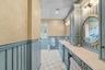 Custom cabinetry featuring beadboard paneling, stone countertops, integrated dual mirrors with decorative frames, wall-mounted lighting fixtures, and 