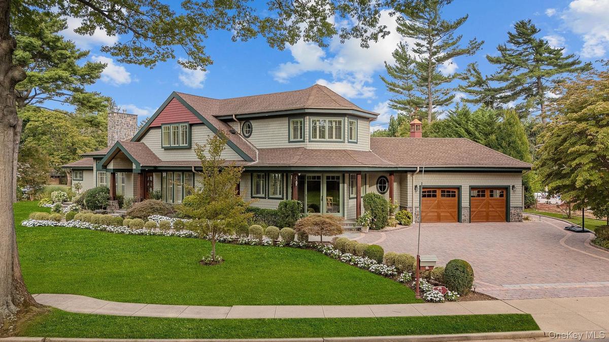 Multi-story residence featuring composite siding with stone veneer accents, an expansive paved driveway, two-car garage with carriage-style doors, and