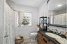 Bathroom featuring white subway tile wall cladding, wood-finish vanity with a dark countertop and integrated sink, large-format framed mirror, and woo