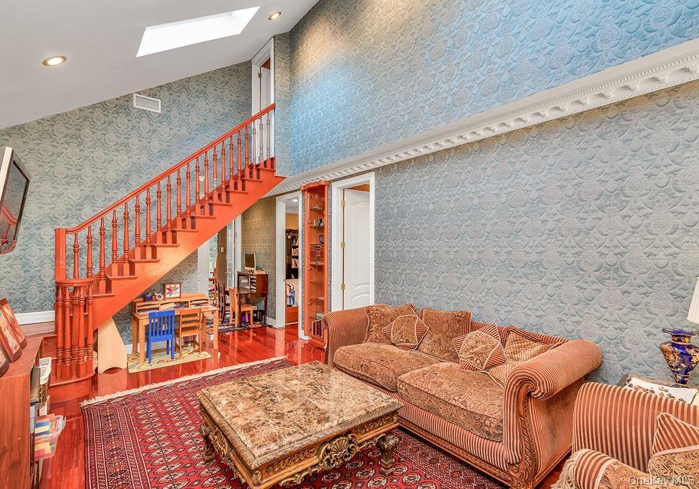 Vaulted ceilings with integrated skylight, mahogany-toned staircase with turned balusters, built-in display cabinetry, crown molding, and polished woo