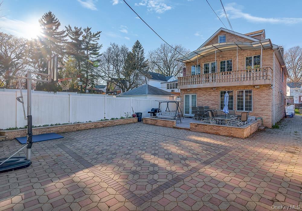 Multi-story brick exterior featuring a second-level balcony with stone balustrade, expansive paved patio, built-in masonry retaining walls, and vinyl 