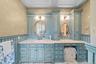Dual-sink vanity featuring custom blue cabinetry, stone countertop, integrated floor-to-ceiling storage towers, beadboard wainscoting, and oval wall m