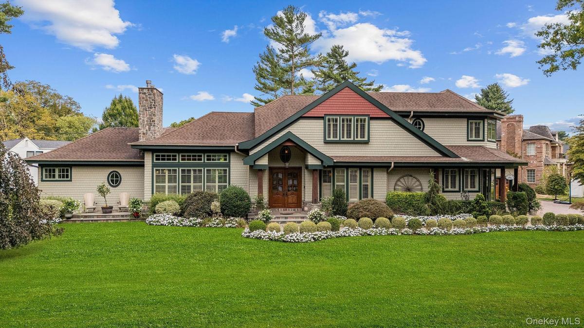 Multi-gabled exterior featuring light-toned shingle siding, contrasting dark window trim, dual stone chimneys, and a covered entryway with double wood