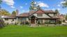 Multi-gabled exterior featuring light-toned shingle siding, contrasting dark window trim, dual stone chimneys, and a covered entryway with double wood