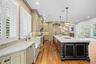 Kitchen featuring custom cabinetry, farmhouse-style sink, wood-finish flooring, stone-surfaced countertops, and a substantial center island