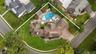 Aerial view featuring a paved driveway, multi-gabled roofline, expansive backyard, in-ground pool, and stone-paver patio