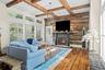 Living room featuring a reclaimed wood accent wall, stone-surround fireplace with a live-edge mantel, exposed timber ceiling beams, wood-finish floori