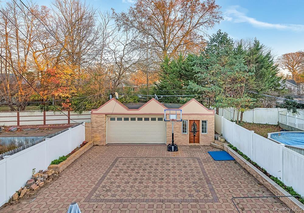 Detached garage with a multi-gabled roofline, brick façade, paved patio, and white vinyl privacy fencing
