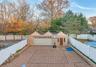 Detached garage with a multi-gabled roofline, brick façade, paved patio, and white vinyl privacy fencing