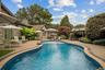 Curved in-ground swimming pool featuring stone-paver decking, a built-in pergola, and stone masonry exterior siding