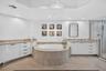 Recessed lighting, a built-in soaking tub with stone surround, a walk-in shower with glass enclosure, white cabinetry, and stone countertops