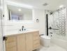Bathroom featuring a light wood vanity with a white countertop, wall-mounted LED-backlit mirror, matte black fixtures, and a glass-enclosed tub with p
